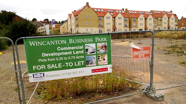 A plot of commerical land up for sale/let, with the New Barns residential development in the background
