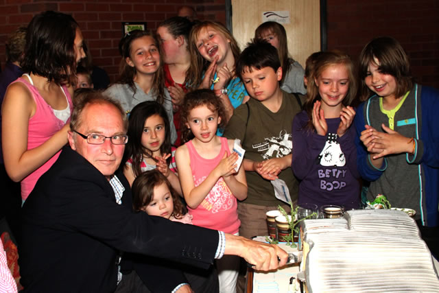 Tim Carroll cuts the magnificent cake, displaying only mild concern about the nearby horde of sugar addicts